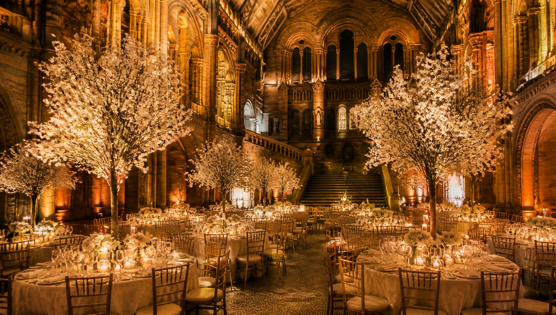 Grand candlelit wedding banquet beneath blossom trees in a historic hall